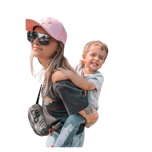 blonde boy being carried by a woman in a pink hat on her back